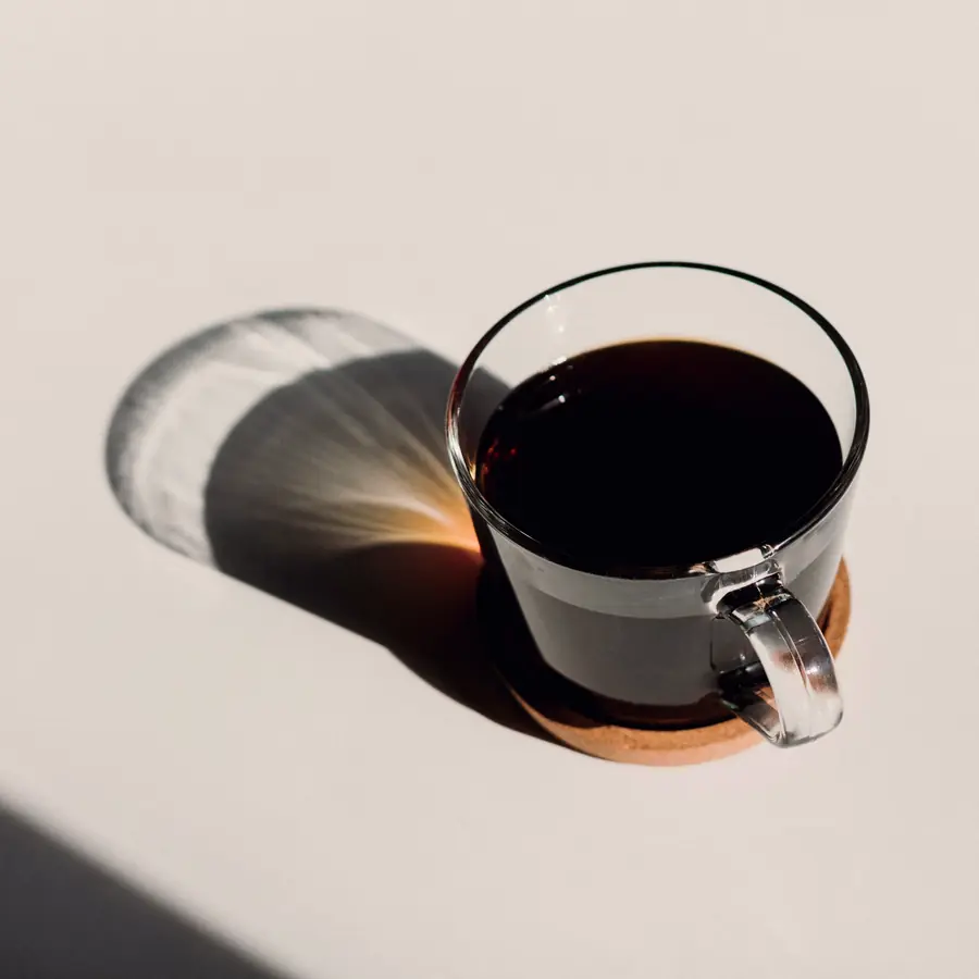 Svart kaffi í glæru bolli, langur skuggi í morgunsól.